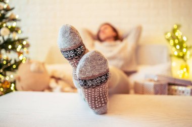 Noel ağacının yanındaki koltukta oturan kadın. Dişi bacaklar, kışın yün çoraplar, masaya koymak ve el yapımı hediye kutuları paketledikten sonra dinlenmek. Aile için hediyeler.