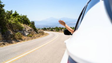 Pencereden elini uzatıp araba kullanan bir kadın. Dağlardaki yılanlı yolda yolculuk. Yaz tatili. Özgürlük kavramı. Boşluğu kopyala