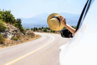 Açık pencereden hasır şapka taşıyan bir kadın. Dağlardaki yılanlı yolda yolculuk. Yaz tatili