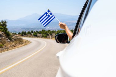 Yunanistan bayrağını açık araba camından tutan kadın dağlardaki serpentin yolda gidiyor. Kavram