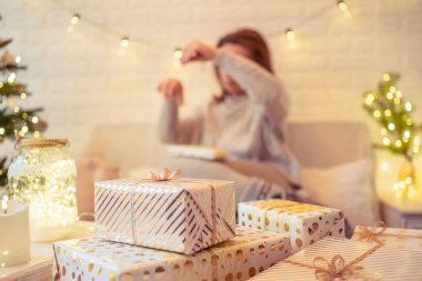 Noel ağacının yanındaki koltukta oturan ve el yapımı hediye kutularını masaya koyan kadın. Aile için hediyeler.