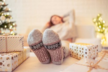 Noel ağacının yanındaki koltukta oturan kadın. Dişi bacaklar, kışın yün çoraplar, masaya koymak ve el yapımı hediye kutuları paketledikten sonra dinlenmek. Aile için hediyeler.