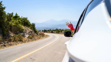 Noel eldivenli kadın açık pencereden elini uzatıp araba kullanıyor. Dağlardaki yılan yolunda gezintiye çıktım..