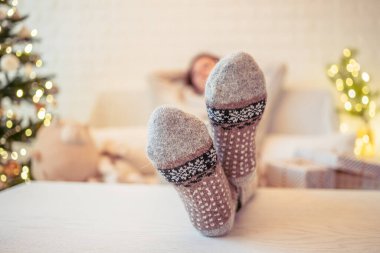 Noel ağacının yanındaki koltukta oturan kadın. Dişi bacaklar, kışın yün çoraplar, masaya koymak ve el yapımı hediye kutuları paketledikten sonra dinlenmek. Aile için hediyeler.