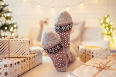 Noel ağacının yanındaki koltukta oturan kadın. Dişi bacaklar, kışın yün çoraplar, masaya koymak ve el yapımı hediye kutuları paketledikten sonra dinlenmek. Aile için hediyeler.