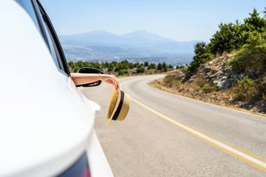 Açık pencereden hasır şapka taşıyan bir kadın. Dağlardaki yılanlı yolda yolculuk. Yaz tatili