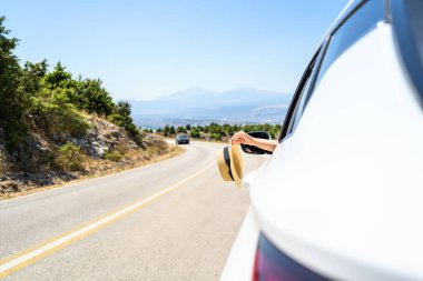 Açık pencereden hasır şapka taşıyan bir kadın. Dağlardaki yılanlı yolda yolculuk. Yaz tatili