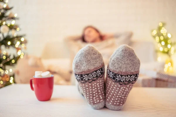 Noel ağacının yanındaki koltukta oturan kadın. Dişi bacaklar, kışın yün çoraplar, masaya koymak ve el yapımı hediye kutuları paketledikten sonra dinlenmek. Aile için hediyeler.