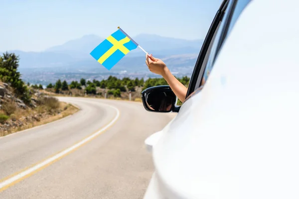 Kobieta Trzymająca Szwedzką Flagę Otwartego Okna Samochodu Jadąca Wzdłuż Drogi — Zdjęcie stockowe