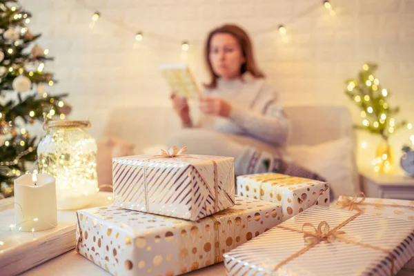 女人坐在圣诞树旁的沙发上 打包着手工制作的礼品盒放在桌上 送给家人的礼物 — 图库照片