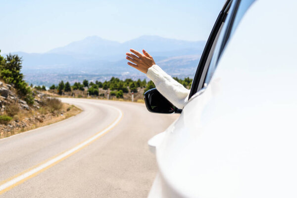 Woman sticking hand out from the open window driving a car. Trip on the serpentine road in the mountains. Summer vacation. Freedom concept. copy space