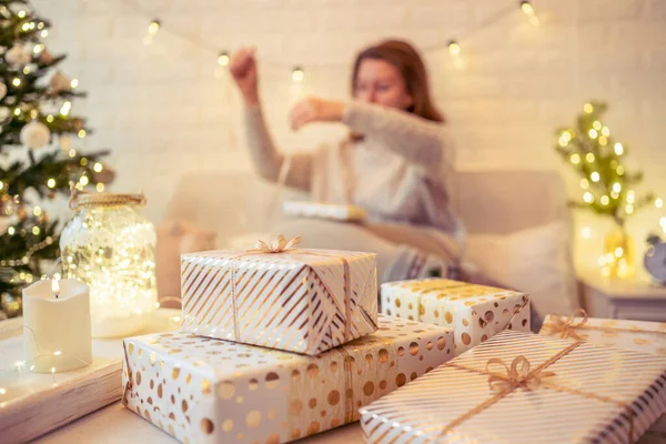 クリスマスツリーの近くのソファに座り 手作りのギフトボックスを梱包してテーブルの上に置きます 家族へのプレゼント — ストック写真
