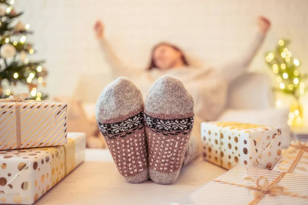 Noel ağacının yanındaki koltukta oturan kadın. Dişi bacaklar, kışın yün çoraplar, masaya koymak ve el yapımı hediye kutuları paketledikten sonra dinlenmek. Aile için hediyeler.