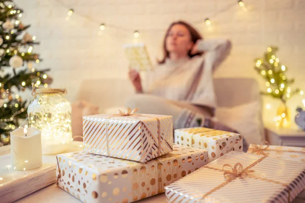 女人坐在圣诞树旁的沙发上 打包着手工制作的礼品盒放在桌上 送给家人的礼物 — 图库照片