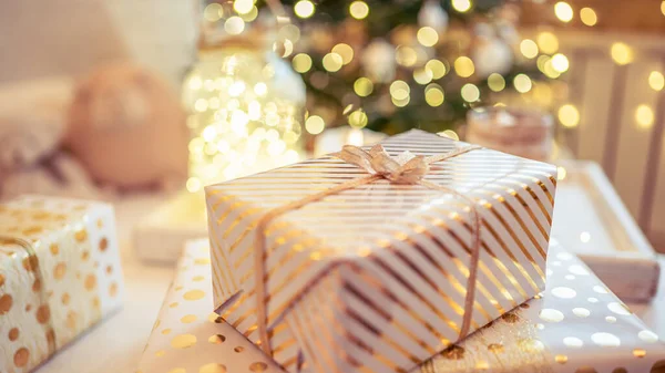 stock image A lot of packing handmade gift boxes lying on the table near Christmas tree in the midst of golden lights, glowing garland, candle. Soft focus. 16:9