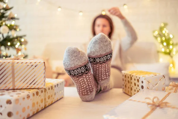 クリスマスツリーの近くのソファに座っている女性 女性の足 冬の足は テーブルの上に置き 手作りのギフトボックスを梱包した後 リラックスしたウールの靴下 家族へのプレゼント — ストック写真