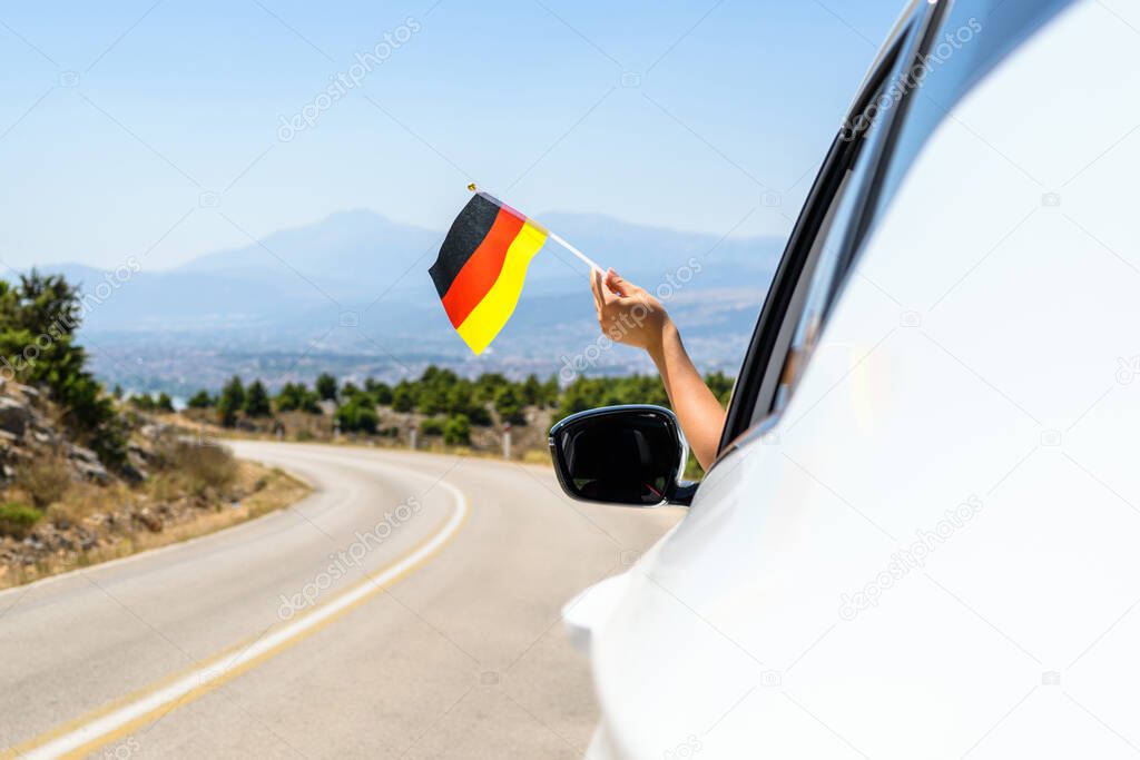 Woman holding Germany flag from the open car window driving along the serpentine road in the mountains. Concept