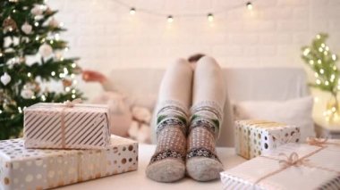 Noel ağacının yanındaki koltukta oturan kadın. Dişi bacaklar, kışın yün çoraplar, masaya koymak ve el yapımı hediye kutuları paketledikten sonra dinlenmek. Aile için hediyeler