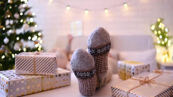 クリスマスツリーの近くのソファに座っている女性 女性の足 冬の足は テーブルの上に置き 手作りのギフトボックスを梱包した後 リラックスしたウールの靴下 家族へのプレゼント — ストック動画
