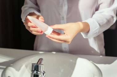 Kadın, koruyucu ve kuru cilt için ellerini yıkadıktan sonra banyoda beyaz lavabonun yanında penceresinden güneş ışığı alarak krem sürüyor.. 