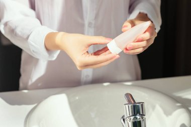 Kadın, koruyucu ve kuru cilt için ellerini yıkadıktan sonra banyoda beyaz lavabonun yanında penceresinden güneş ışığı alarak krem sürüyor.. 