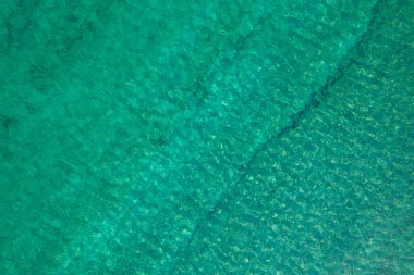 Background, texture of relaxing, calm turquoise, transparent sea water with stones, slabs, lump, coral. Summer vacation. Blue ocean lagoon. Drone, copter top view. 