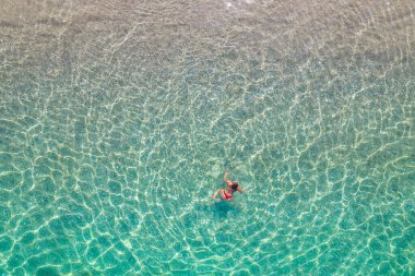 Üst, hava manzaralı. Kumsalda deniz suyunda yüzen kırmızı bikinili genç bir kadın. Drone, helikopter fotoğrafı. Yaz tatili. Yukarıdan görüntüle. 