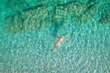 Üst, hava manzaralı. Şapkalı ve kumsalda deniz suyunda yüzen beyaz bikinili güzel bir kadın. Drone, helikopter fotoğrafı. Yaz tatili. Yukarıdan görüntüle. 