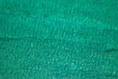 Background, texture of relaxing, calm turquoise, transparent sea water with stones, slabs, lump, coral. Summer vacation. Blue ocean lagoon. Drone, copter top view. 