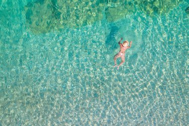 Top, aerial view. Young beautiful woman in a hat and white bikini swimming in sea water on the sand beach. Drone, copter photo. Summer vacation. View from above. 