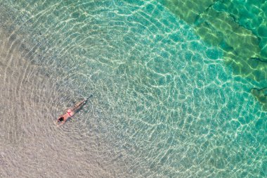 Üst, hava manzaralı. Kırmızı bikinili genç bir kadın kumsalda deniz suyunda güneşleniyor. Drone, helikopter fotoğrafı. Yaz tatili. Yukarıdan görüntüle. 