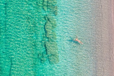 Top view. Young beautiful naked woman in a hat swimming in sea water on sand beach. Drone, copter photo. Summer vacation. View from above. 