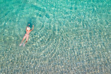 Top, aerial view. Young beautiful woman in a hat and white bikini swimming in sea water on the sand beach. Drone, copter photo. Summer vacation. View from above. 