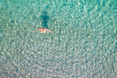 Top view. Young beautiful naked woman in a hat standing and sunbathe in sea water. Drone, copter photo. Summer vacation. View from above