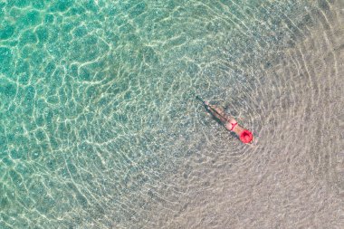 Üst Manzara. Kırmızı şapkalı ve bikinili genç bir kadın kumsalda deniz suyunda güneşleniyor. Drone, helikopter fotoğrafı. Yaz tatili. Yukarıdan görüntüle. 