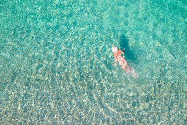 Top, aerial view. Young beautiful woman in a hat and white bikini swimming in sea water on the sand beach. Drone, copter photo. Summer vacation. View from above. 