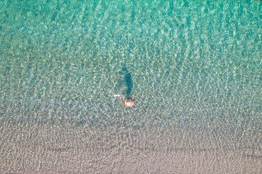 Top view. Young beautiful naked woman in a hat taking off bikini in sea water. Drone, copter photo. Summer vacation. View from above.