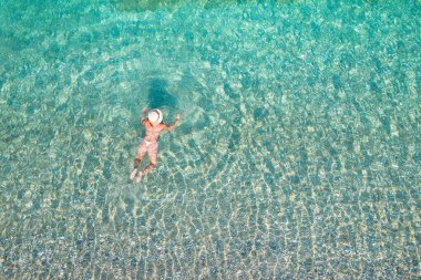 Top, aerial view. Young beautiful woman in a hat and white bikini swimming in sea water on the sand beach. Drone, copter photo. Summer vacation. View from above. 