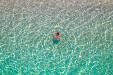 Üst, hava manzaralı. Kumsalda deniz suyunda yüzen kırmızı bikinili genç bir kadın. Drone, helikopter fotoğrafı. Yaz tatili. Yukarıdan görüntüle. 