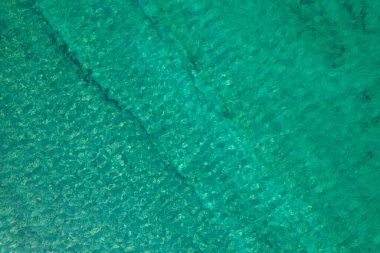 Background, texture of relaxing, calm turquoise, transparent sea water with stones, slabs, lump, coral. Summer vacation. Blue ocean lagoon. Drone, copter top view. 