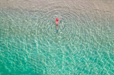 Top view. Young beautiful woman in a red hat and bikini lying and sunbathe in sea water on the sand beach. Drone, copter photo. Summer vacation. View from above. 