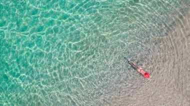 Üst Manzara. Kırmızı şapkalı ve bikinili genç bir kadın kumsalda deniz suyunda güneşleniyor. Drone, helikopter fotoğrafı. Yaz tatili. Yukarıdan görüntüle. 