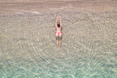 Top, aerial view. Young beautiful woman in a red bikini panties lying and sunbathe in sea water on the sand beach. Drone, copter photo. Summer vacation. View from above. 