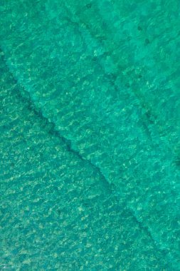Background, texture of relaxing, calm turquoise, transparent sea water with stones, slabs, lump, coral. Summer vacation. Blue ocean lagoon. Drone, copter top view. 