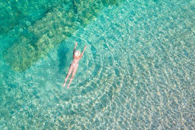 Top, aerial view. Young beautiful woman in a hat and white bikini swimming in sea water on the sand beach. Drone, copter photo. Summer vacation. View from above. 