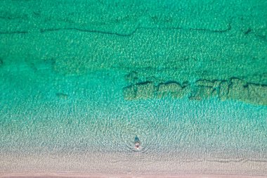 Top, aerial view. Young beautiful woman in a hat and white bikini swimming in sea water on the sand beach. Drone, copter photo. Summer vacation. View from above. 