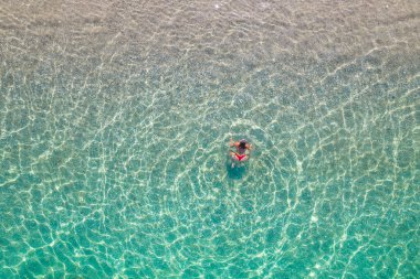 Üst, hava manzaralı. Kumsalda deniz suyunda yüzen kırmızı bikinili genç bir kadın. Drone, helikopter fotoğrafı. Yaz tatili. Yukarıdan görüntüle. 