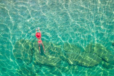 Top view. Young beautiful woman in a red hat and bikini swimming in sea water on the sand beach. Drone, copter photo. Summer vacation. View from above. 