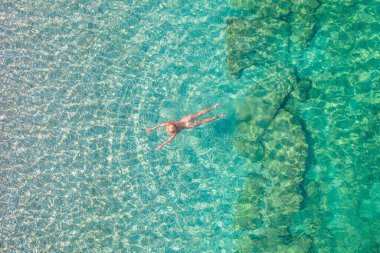 Top view. Young beautiful naked woman in a hat swimming in sea water on sand beach. Drone, copter photo. Summer vacation. View from above. 