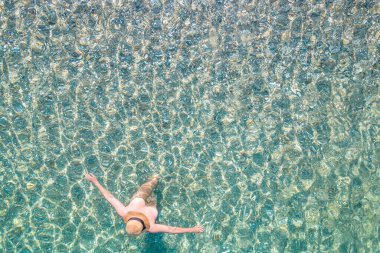 Top view. Young beautiful naked woman in a hat standing and sunbathe in sea water. Drone, copter photo. Summer vacation. View from above